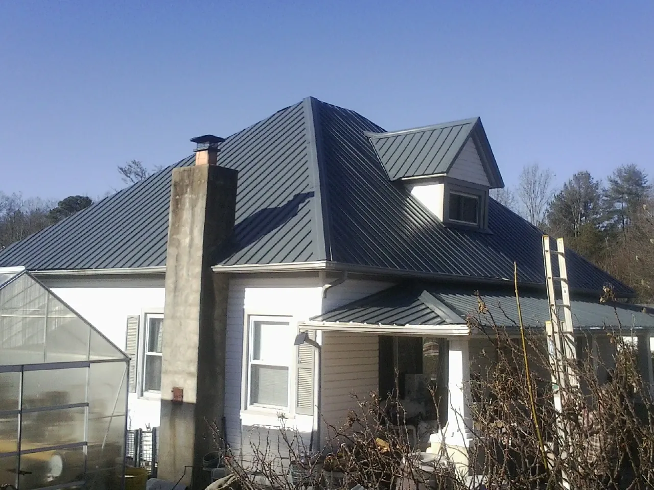 Dark blue standing seam metal roof on a white farmhouse with dormer — Slate & Tile Roof Repair by Roofing Brothers in Provincetown
