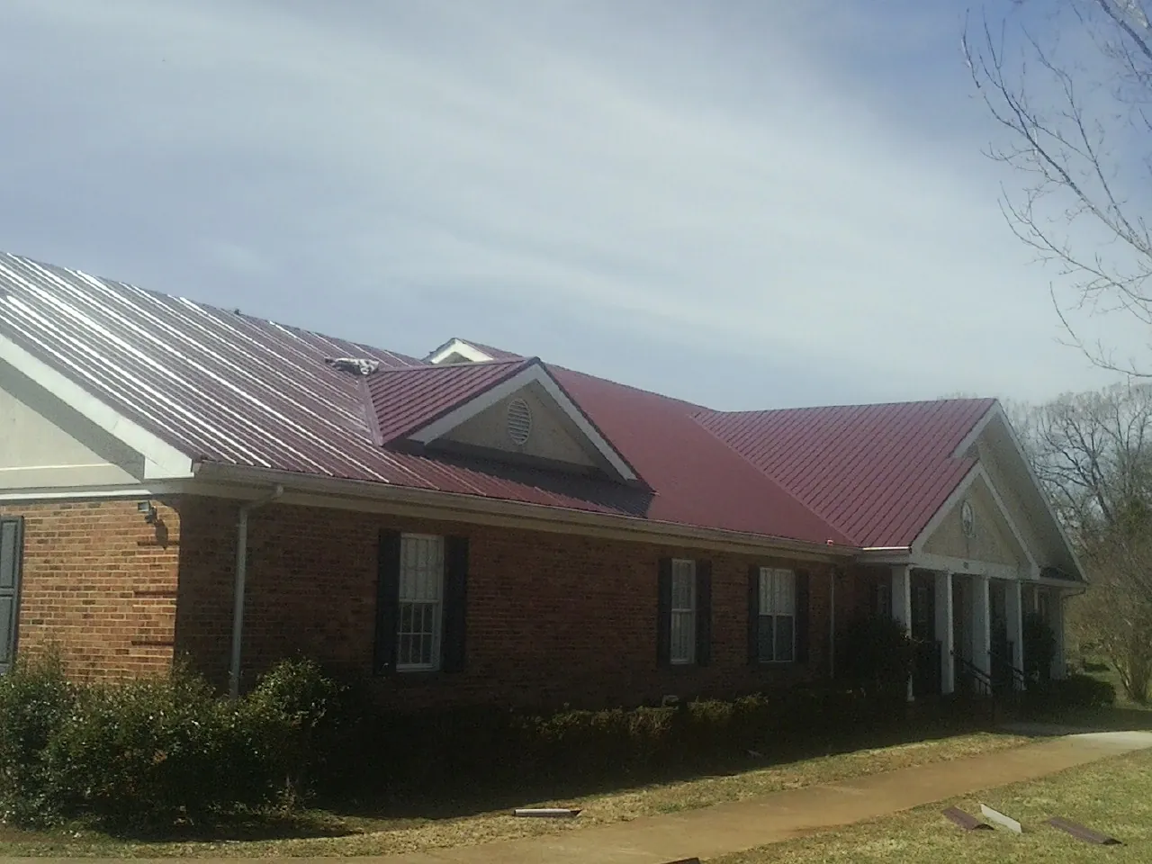 Red metal roof with gabled entries on a long brick building, from a Hail Damage Roof Repair job in Provincetown