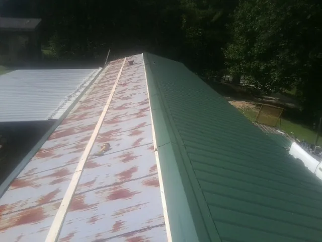 Old rusted panels beside newly installed green metal roofing — Wind Damage Roof Repair by Roofing Brothers in Provincetown