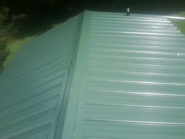 New green metal panels meeting at the ridge of a roof — Flat Roof Repair work by our crew in Provincetown