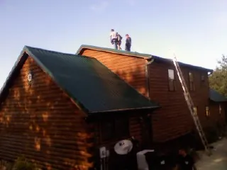 Crew on the ridge of a green metal roof on a two story log home in Provincetown