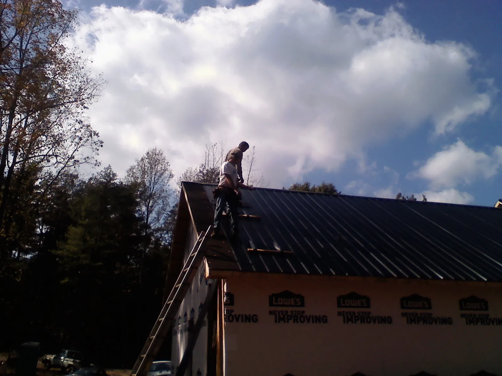 Roofer fastening dark metal panels high against a cloudy sky, from a Roof Inspection job in Provincetown