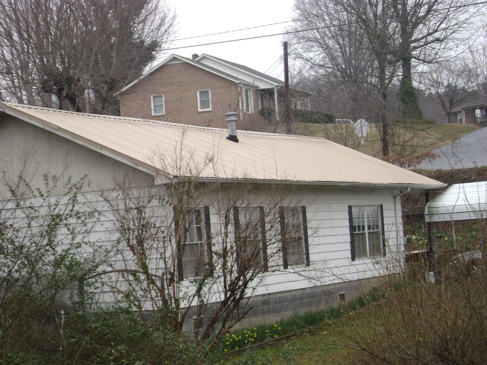Tan metal roof on a white sided house set into a hillside — Commercial Roofing by Roofing Brothers in Provincetown
